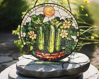 May include: A stained glass window hanging with a depiction of green cucumbers in a basket with yellow flowers and a sun.
