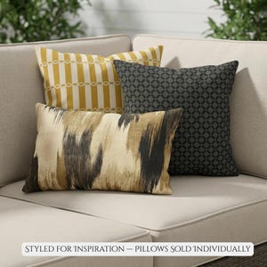 May include: Four decorative cushions on a beige sofa. Designs include yellow and white stripes, a black geometric pattern, and a beige and black abstract pattern. Text at the bottom reads: STYLED FOR INSPIRATION - PILLOWS SOLD INDIVIDUALLY.