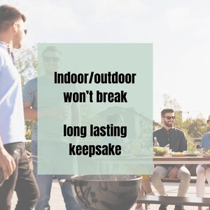May include: A black charcoal grill with a round shape is in the foreground. The image includes the text "Indoor/outdoor won't break long lasting keepsake". Several people are gathered around a table in the background.