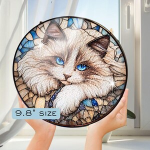 May include: A stained glass round wall decor featuring a white cat with blue eyes. The cat is surrounded by a mosaic of blue, brown, and white glass pieces. The text "9.8" SIZE is printed below the image.