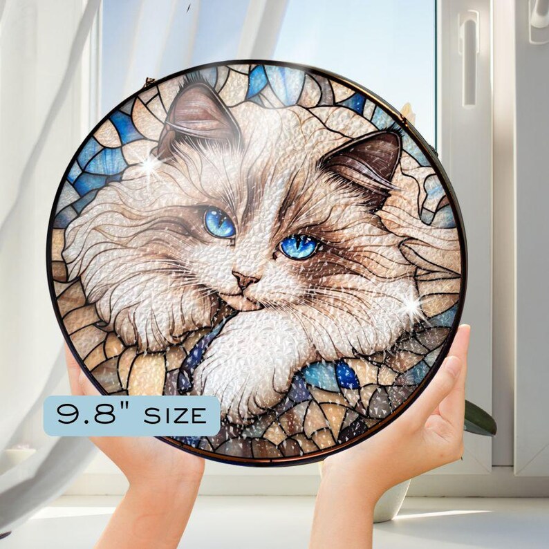May include: A stained glass round wall decor featuring a white cat with blue eyes. The cat is surrounded by a mosaic of blue, brown, and white glass pieces. The text "9.8" SIZE is printed below the image.