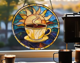 May include: A round stained glass window depicting a coffee cup with steam rising, set against a sunburst design. The artwork features shades of yellow, blue, and brown, hanging in front of a window. A coffee maker and a mug are in the foreground.