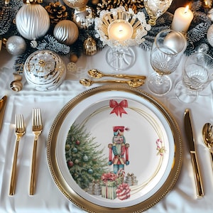 Op de afbeelding: Een feestelijke kersttafelsetting met een wit tafelkleed, gouden bestek en decoraties. Het middelpunt is een bord met een gouden rand, met een kerstboom en notenkraker ontwerp. Kaarsen en glazen maken de scène compleet.