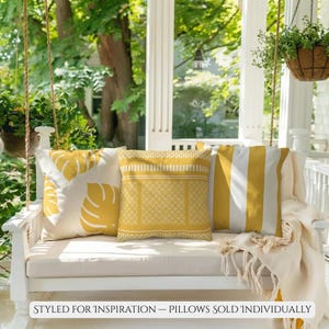 May include: Three decorative throw pillows in shades of yellow and white rest on a white swing. One pillow features a leaf pattern, another a geometric design, and the third has vertical stripes. The text at the bottom reads "STYLED FOR INSPIRATION - PILLOWS SOLD INDIVIDUALLY."