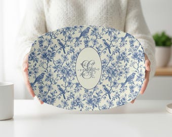 May include: Oval serving platter with a blue and white floral and bird pattern. The platter has a cream-colored background with blue flowers, birds, and branches. An oval in the center features a floral monogram.