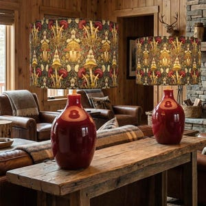 May include: Two matching table lamps with red bases and patterned shades. The shades feature a repeating design of mushrooms in shades of yellow, red, and green. The lamps are placed on a rustic wooden table in a cozy living room setting.