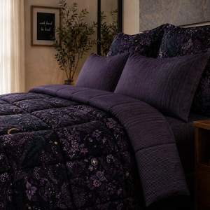 May include: A dark purple comforter set featuring a floral and botanical pattern with small gold stars. The bedding includes matching pillow shams with a fine pinstripe texture on one side and a coordinating floral print on the other side.