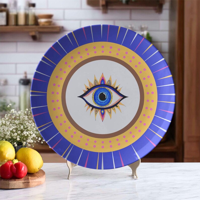 Dinner plate with evil eye design in blue, gold, and purple, placed on display stand on a kitchen counter