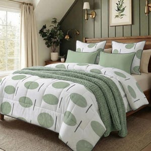 May include: A bed with a white comforter featuring a green oval pattern and black lines. The bed has green pillows and a green knitted throw blanket. The bed frame is wooden.