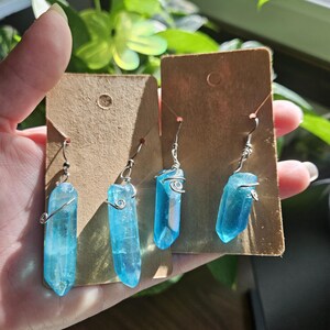 May include: Four blue crystal earrings with silver wire wrapped around the top of each crystal. The earrings are displayed on two brown card stock earring display cards.