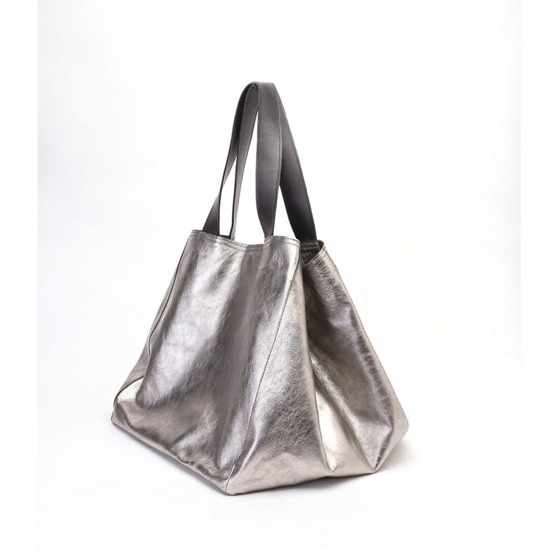 Extra-large silver leather tote bag with a slouchy, oversized design. The bag is made from metallic leather and features reinforced black leather handles for carrying on the shoulder or by hand. Its lightweight structure and spacious interior make it a stylish and practical choice for everyday use.
