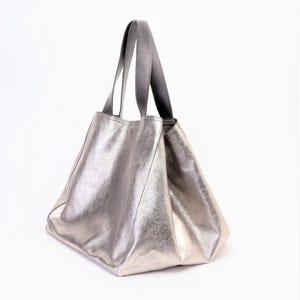 Puede incluir: Un bolso tote de cuero plateado con asas de cuero negro.