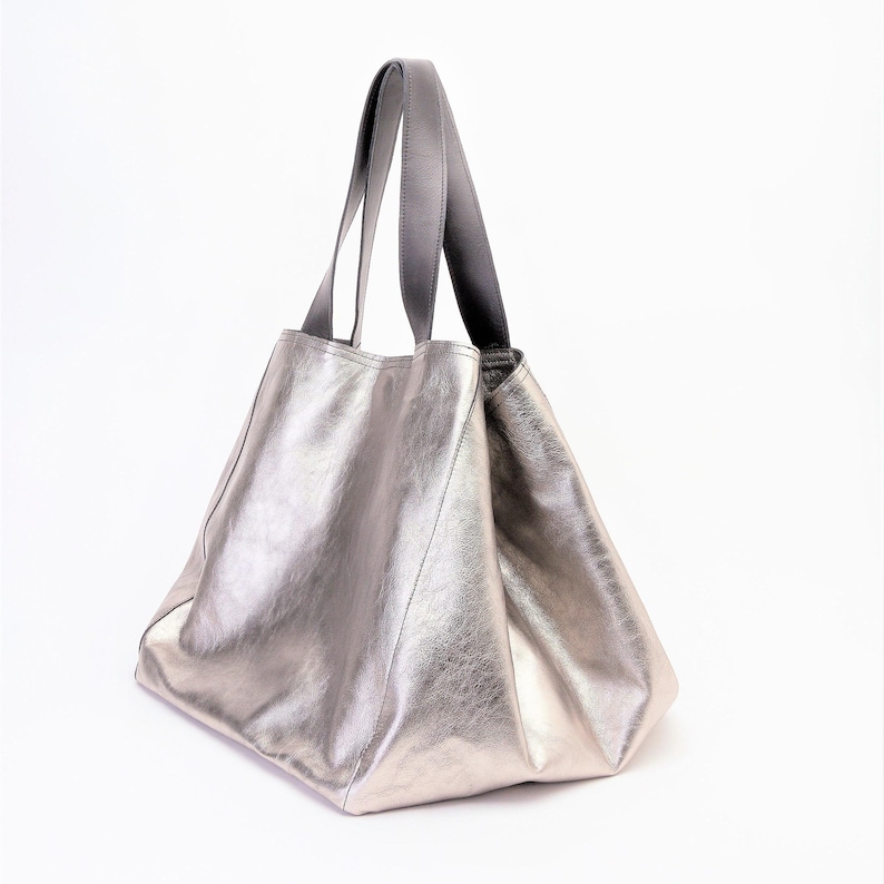Puede incluir: Un bolso tote de cuero plateado con asas de cuero negro.