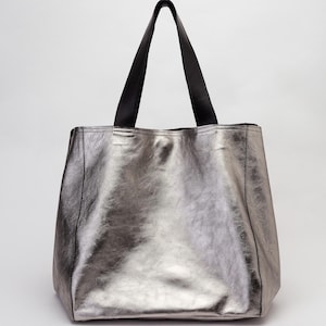 Puede incluir: Un bolso tote met&aacute;lico plateado con asas de cuero negro.