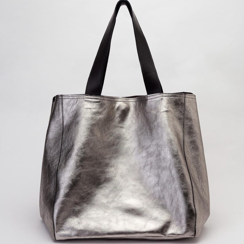Puede incluir: Un bolso tote met&aacute;lico plateado con asas de cuero negro.