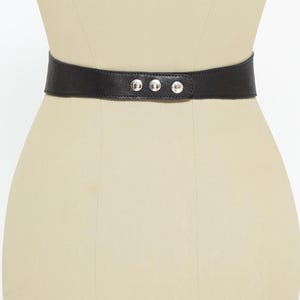 May include: A black leather belt with three silver-colored rivets. The belt is wide and cinches at the waist. The belt is displayed on a mannequin.