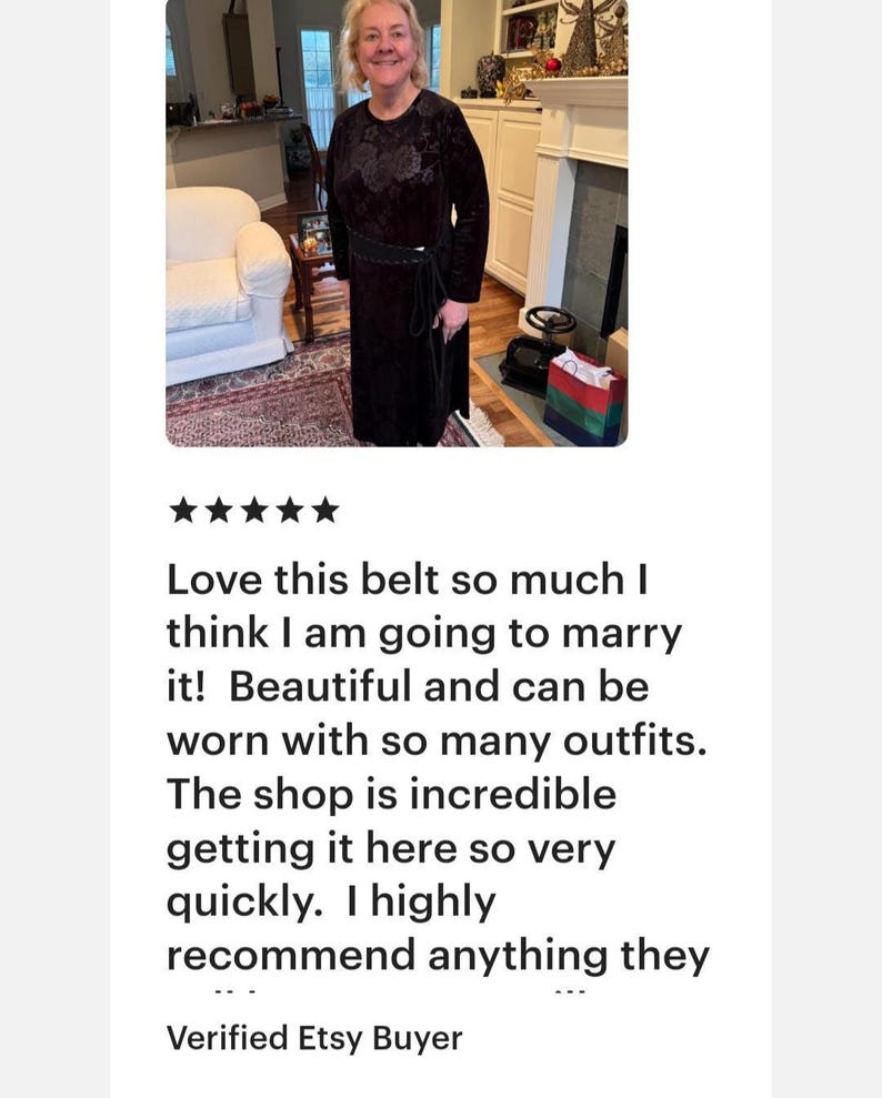 May include: A black belt featuring a textured, patterned surface and a thin, wrap-around tie closure. The belt is worn over a long-sleeved, dark-colored dress with a subtle floral pattern, creating a cinched waist effect with the tie.