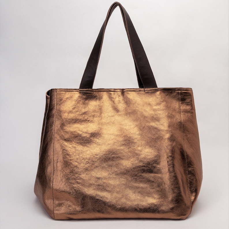 May include: A large, metallic bronze tote bag with brown leather handles.