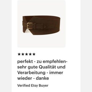 May include: A wide, dark brown waist belt featuring a matte finish and a structured, contoured shape. The belt includes a horizontal strap across the front secured by a rectangular, metallic-toned buckle, creating a cinched appearance.