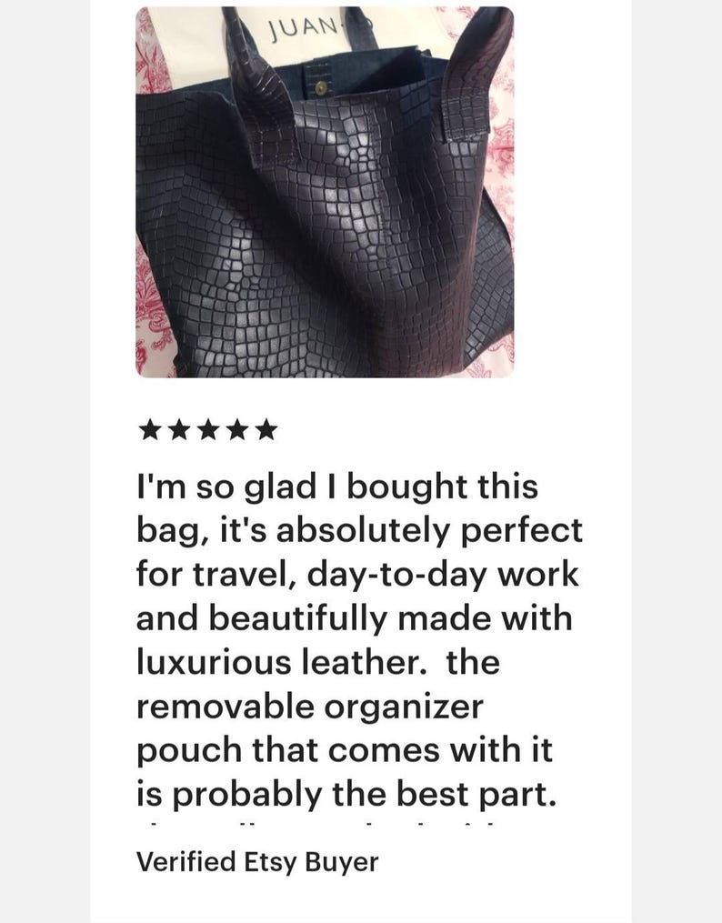 May include: A dark navy blue tote bag with a textured crocodile skin pattern, featuring two sturdy shoulder straps and a visible snap button closure at the top. The interior contains a light-colored fabric pouch with the text JUAN visible.