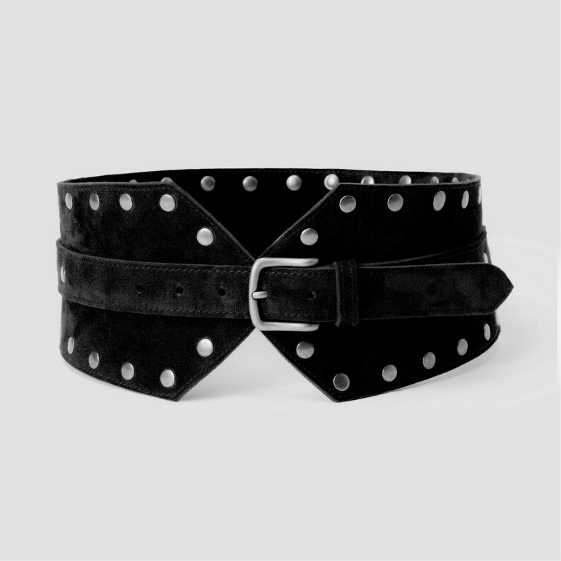 May include: A wide black belt featuring a suede-like texture, adorned with rows of silver-toned metal studs along the top and bottom edges. The belt includes a central horizontal strap with a matching silver-toned metal buckle and prong closure.