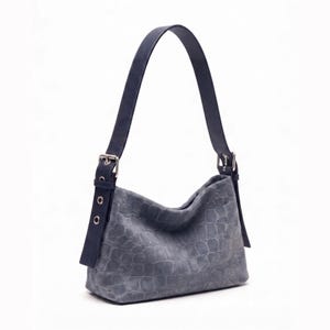 May include: A slate gray shoulder bag featuring a textured crocodile skin pattern. The bag includes a single dark blue strap attached with silver-toned metal buckles on each side, which feature adjustable eyelets for a secure and functional design.
