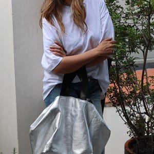 May include: A silver leather tote bag with black straps. The bag is large and has a slouchy, relaxed look.