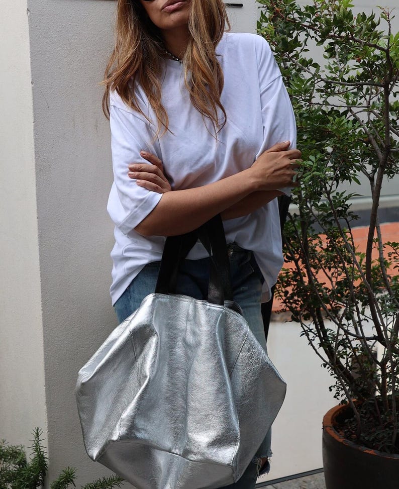 May include: A silver leather tote bag with black straps. The bag is large and has a slouchy, relaxed look.