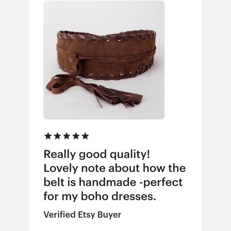 May include: A wide brown suede belt featuring a dark brown leather whipstitch detail along the top and bottom edges. The belt includes long, thin suede tie straps that hang down, ending in a series of fringe tassels at the ends of the ties.