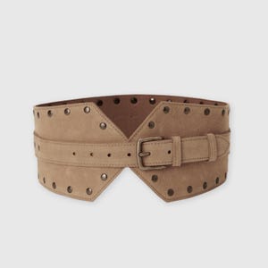 May include: A wide tan suede belt featuring a central strap with a metal buckle and a series of evenly spaced metal studs along the top and bottom edges. The belt has a distinct angular shape that tapers toward the center buckle closure.