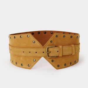 May include: A wide mustard yellow suede belt featuring a central buckle closure and a series of metallic studs along the top and bottom edges. The belt has a structured, contoured shape with a horizontal strap overlay across the middle section.