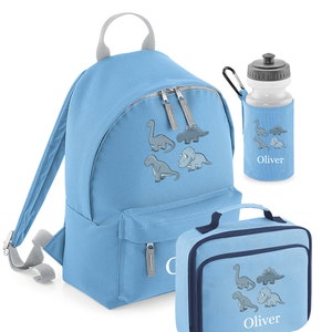 May include: A light blue backpack, lunch bag, and water bottle set. Each item features a gray dinosaur graphic and the name "Oliver". The backpack has a top handle and adjustable straps. The lunch bag has a handle and a zipper closure. The water bottle has a black cap.