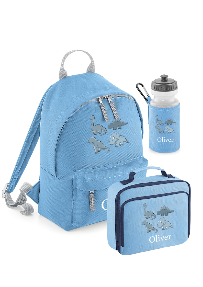 May include: A light blue backpack, lunch bag, and water bottle set. Each item features a gray dinosaur graphic and the name "Oliver". The backpack has a top handle and adjustable straps. The lunch bag has a handle and a zipper closure. The water bottle has a black cap.