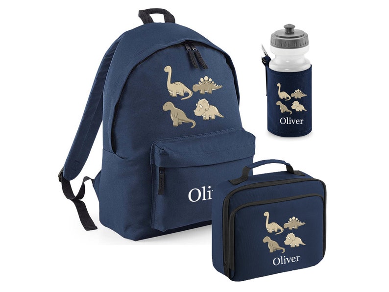 May include: Navy blue backpack, lunch bag, and water bottle set. Each item features a beige dinosaur design and the name "Oliver" in white. The backpack has two zippered compartments and adjustable straps. The lunch bag has a handle.