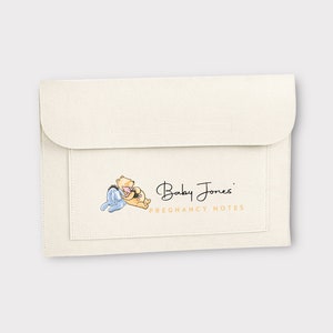 May include: A white felt folder with a pocket on the front. The pocket features an illustration of Winnie the Pooh and Piglet, and the text "Baby Jones' Pregnancy Notes".