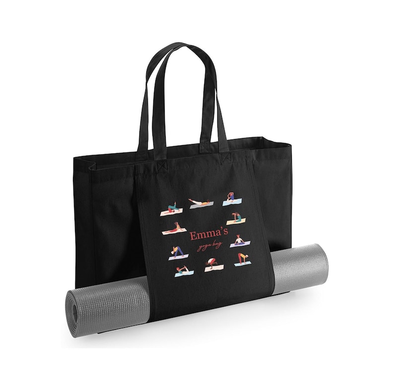 May include: A black tote bag with two handles and a gray yoga mat inserted through the front pocket. The bag features a graphic print of various yoga poses arranged in a circle around the text "Emma's yoga bag" in red and white lettering.