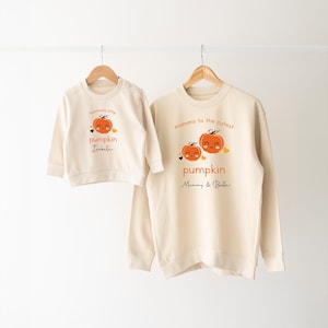 May include: Two cream-colored sweatshirts with pumpkin designs. The larger sweatshirt says "mamma to the cutest pumpkin Mommy & Belle". The smaller sweatshirt says "mommy's little pumpkin Isabelle".
