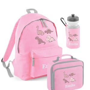 May include: Pink backpack, lunch bag, and water bottle set. Each item features a dinosaur graphic and the name "Emilia". The backpack has a front pocket and gray trim. The water bottle has a black cap.
