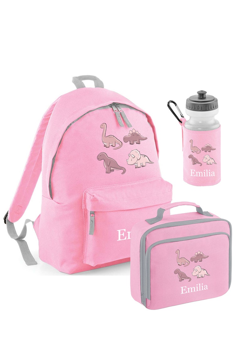 May include: Pink backpack, lunch bag, and water bottle set. Each item features a dinosaur graphic and the name "Emilia". The backpack has a front pocket and gray trim. The water bottle has a black cap.