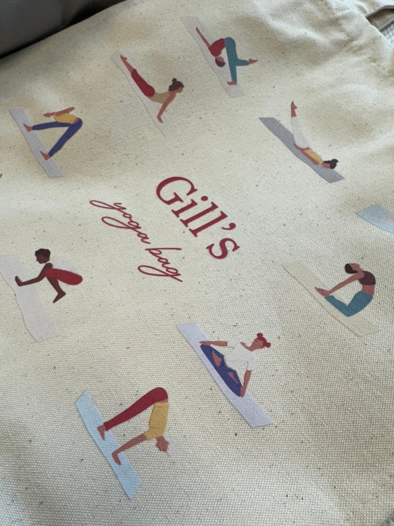 May include: A beige canvas tote bag featuring a repeating pattern of figures in various yoga poses on mats. The center of the bag displays the red text "Gill's yoga bag" in a combination of bold block lettering and a cursive script font.