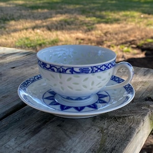 May include: A white teacup and saucer with a blue and white floral pattern. The cup has a scalloped rim and a handle. The saucer has a matching pattern.