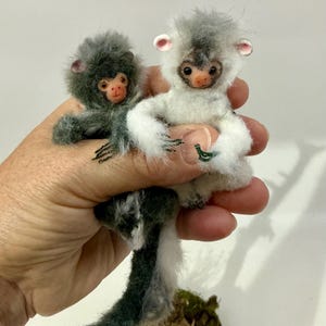 May include: Two miniature primate figurines crafted with soft, fuzzy faux fur. One figurine is dark charcoal gray, while the other is white with gray accents. Both have small, detailed faces with pinkish noses, dark eyes, and rounded ears.
