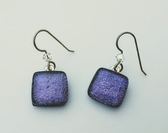 May include: A pair of purple square glass earrings with silver accents. The earrings are on a white background.