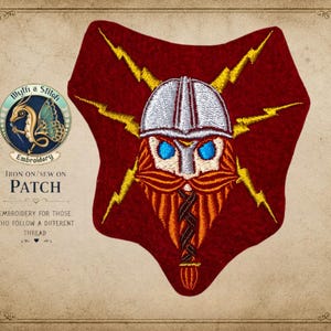 May include: Embroidered patch featuring a Viking warrior with a silver helmet, blue eyes, and a red beard. The patch is shield-shaped with yellow lightning bolts and the text "IRON ON/SEW ON PATCH". The patch is from "Myth & Stitch Embroidery".