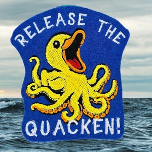 May include: A blue felt patch with white embroidered text that reads "Release the Quacken!" and a yellow embroidered cartoon duck with an octopus body.