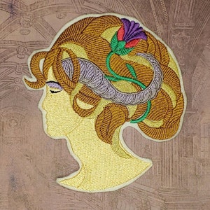 May include: Embroidered patch featuring a woman's profile with a stylized floral design in her hair. The hair is brown, the flower is purple, red, and green, and the woman's face is yellow.