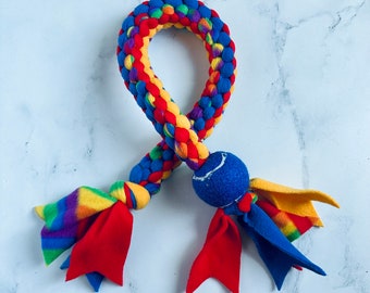 May include: A colorful dog toy featuring a braided rope design in red, yellow, blue, and green. The toy has a blue ball and fabric streamers in rainbow colors and red. This durable toy is designed for interactive play.