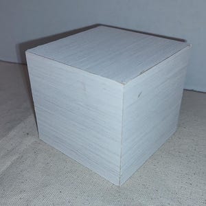 May include: A white wooden cube with a smooth, slightly textured surface.
