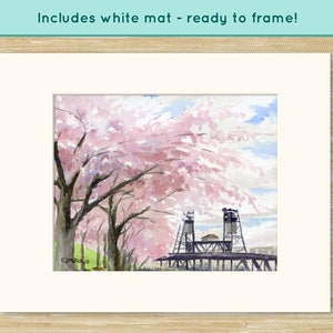 May include: Watercolor painting of a bridge with pink cherry blossoms in the foreground. The bridge is made of metal and has two towers. The painting is framed and includes a white mat.