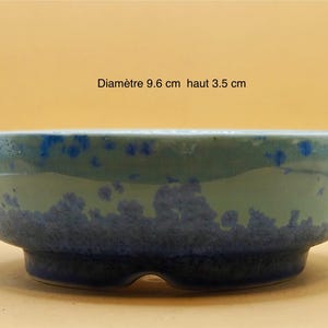 Puede incluir: Un cuenco de cerámica de 9,6 cm de diámetro y 3,5 cm de altura. El cuenco presenta un diseño de dos tonos, con una sección superior verde claro y una sección inferior azul oscuro. Las motas azules añaden detalles.